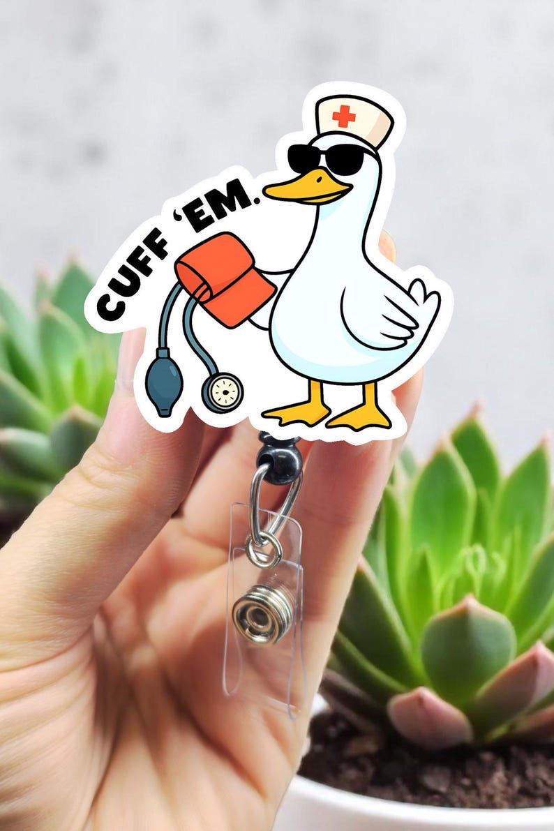 May include: A white sticker featuring a cartoon goose wearing sunglasses and a nurse's hat with a red cross. The goose holds a blood pressure cuff and the text "CUFF 'EM." is above the goose. The sticker is attached to a retractable badge reel.