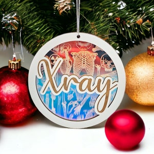 May include: A round Christmas ornament with the word "Xray" in a cursive font. The ornament has a white border and a laser-cut design of a skeleton. The background is a gradient of red, orange, and blue. The ornament is hanging from a silver string.
