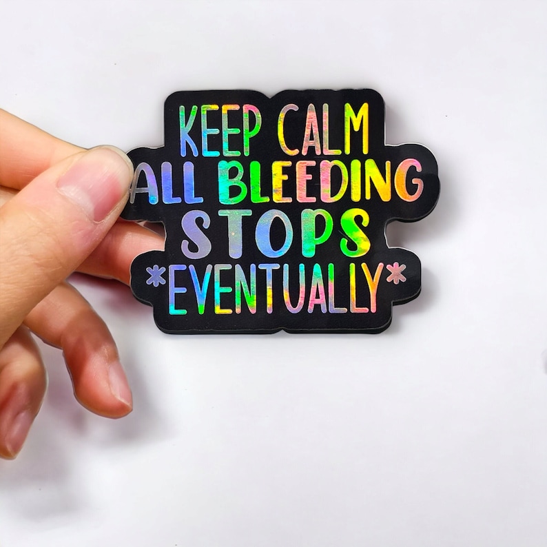 May include: A black sticker with a rainbow holographic finish. The sticker says "Keep Calm All Bleeding Stops *Eventually*"