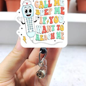 May include: A white badge reel with a cartoon telephone design. The design includes the text "CALL ME BEEP ME IF YOU WANT TO REACH ME" in colorful bubble letters. The reel has a clear plastic strap and a metal clip.