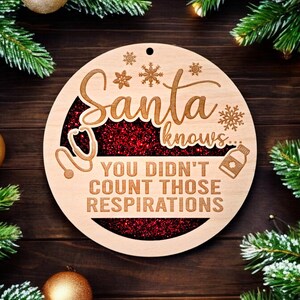 May include: A round wooden Christmas ornament with the words "Santa knows... You didn't count those respirations." The ornament has a red glitter center and snowflake and medical symbol designs. The ornament is surrounded by Christmas decorations.