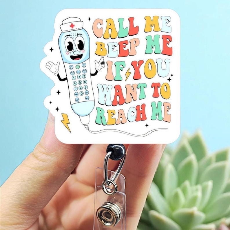 May include: A white and square badge reel with a cartoon telephone character wearing a nurse's hat. The text on the badge reel says "CALL ME BEEP ME IF YOU WANT TO REACH ME" in colorful retro lettering.