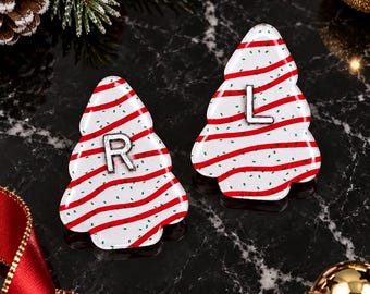May include: Two Christmas tree-shaped ornaments featuring a white base with red wavy horizontal stripes and small green speckles. One ornament displays a silver letter R, and the other displays a silver letter L centered on the front surface.