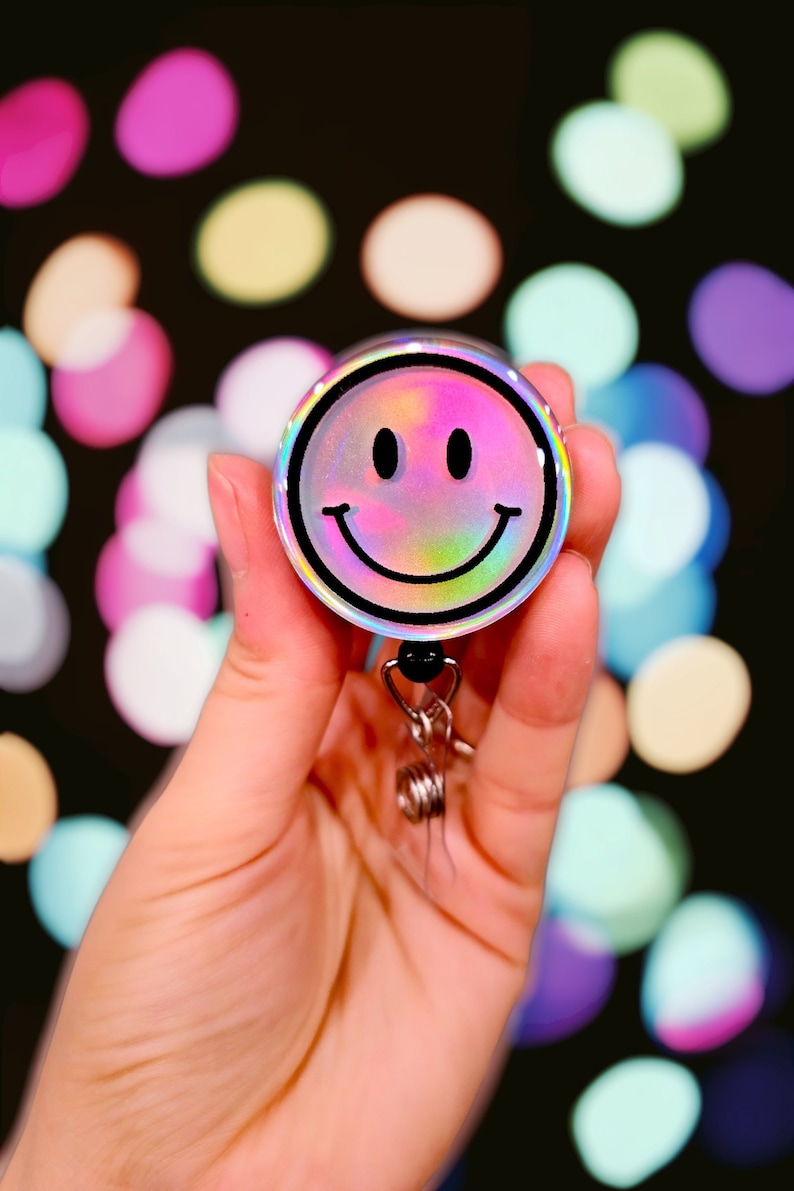 May include: A holographic iridescent smiley face badge reel with a black border and a silver retractable cord.