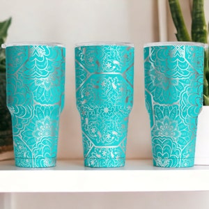 May include: Three turquoise tumblers with silver mandala designs. The tumblers are on a white shelf.