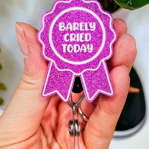 May include: Pink glitter badge holder with a white ribbon and the text "Barely Cried Today".