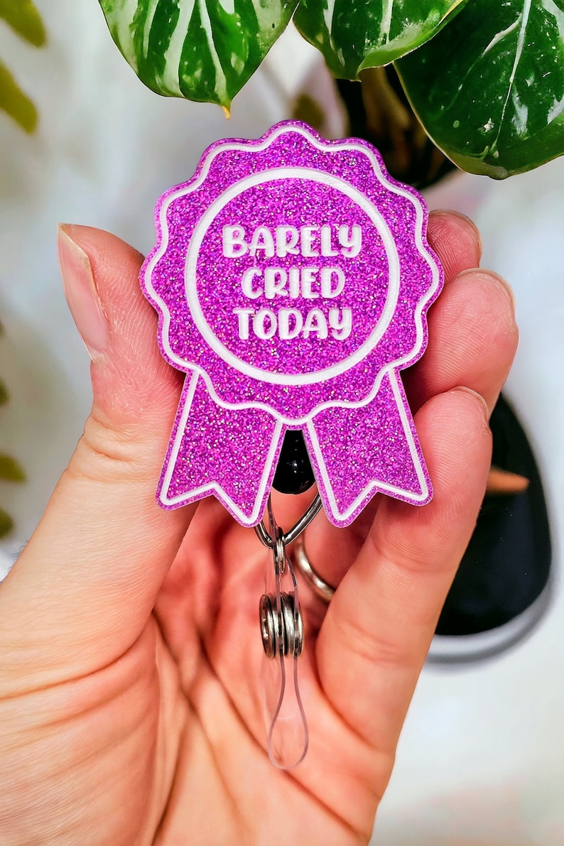 May include: Pink glitter badge holder with a white ribbon and the text "Barely Cried Today".