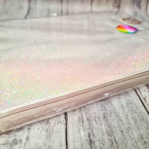 May include: A stack of white iridescent glitter paper wrapped in clear plastic. The paper has a subtle shimmer and is perfect for crafting projects.