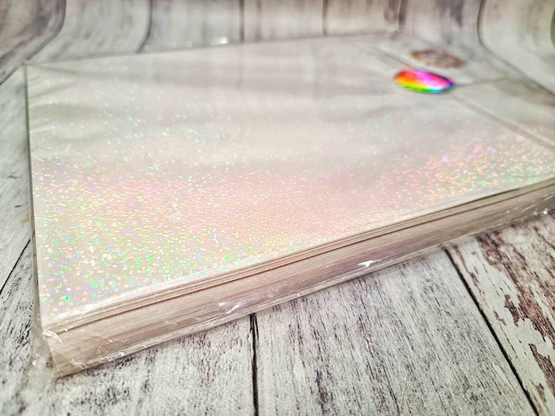 May include: A stack of white iridescent glitter paper wrapped in clear plastic. The paper has a subtle shimmer and is perfect for crafting projects.