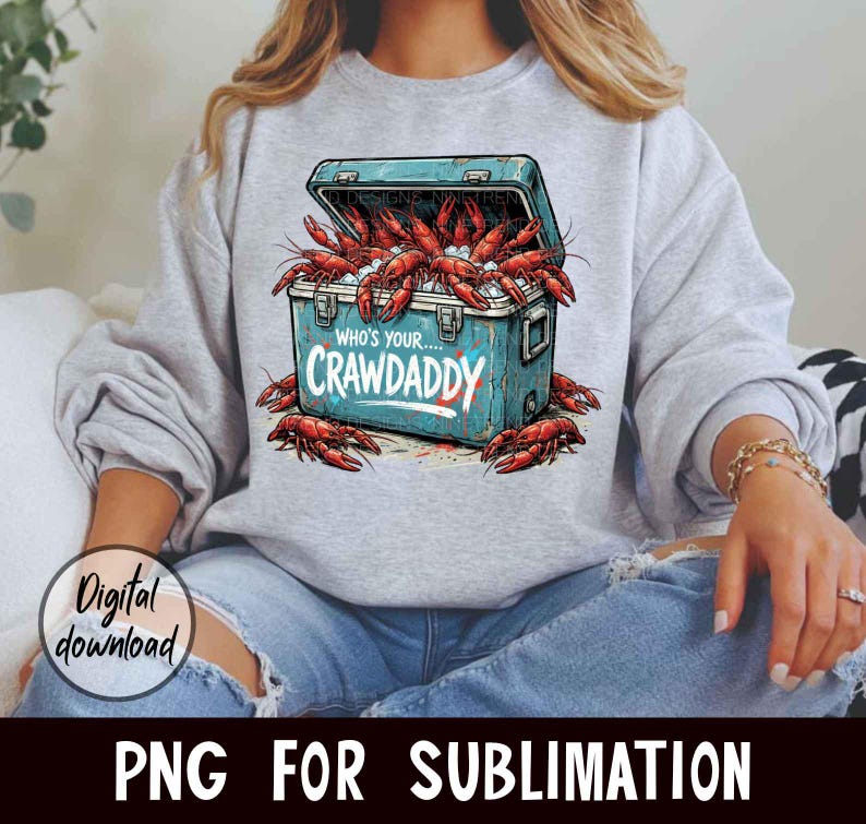 Puede incluir: Una sudadera gris claro con un gr&aacute;fico de una nevera azul desbordante de cangrejos rojos. El texto "WHO'S YOUR...CRAWADDY" est&aacute; impreso en la nevera. Tambi&eacute;n se ven las palabras "Digital download" y "PNG FOR SUBLIMATION".