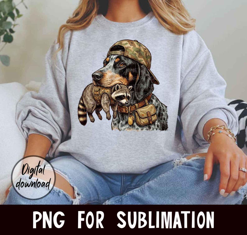 May include: A gray sweatshirt featuring a graphic of a dog wearing a camouflage cap and holding a raccoon. The dog has a brown leather collar and a small bag. The words "Digital download" and "PNG FOR SUBLIMATION" are also visible.