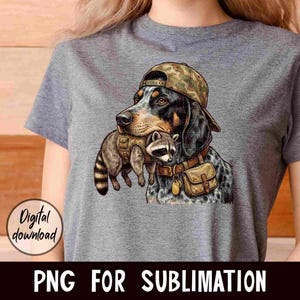 May include: A gray t-shirt featuring a graphic of a dog wearing a camouflage hat and carrying a raccoon. The dog has black and brown fur with blue spots. The raccoon is wearing a vest. Text on the image says "Digital download" and "PNG FOR SUBLIMATION."