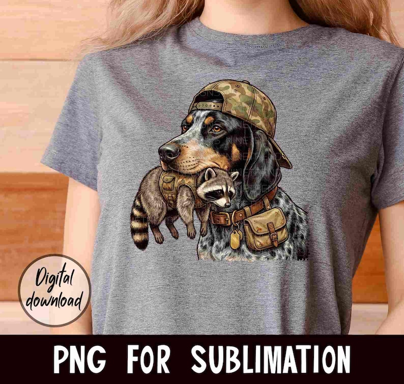 May include: A gray t-shirt featuring a graphic of a dog wearing a camouflage hat and carrying a raccoon. The dog has black and brown fur with blue spots. The raccoon is wearing a vest. Text on the image says "Digital download" and "PNG FOR SUBLIMATION."