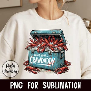 Puede incluir: Sudadera blanca con un gr&aacute;fico de una nevera azul desbordante de cangrejos rojos. La nevera tiene el texto "WHO'S YOUR...CRAWDADDY". Tambi&eacute;n son visibles las palabras "Digital download" y "PNG FOR SUBLIMATION".