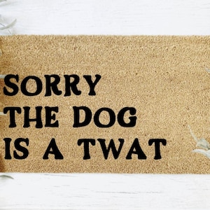 K&ouml;nnte beinhalten: Eine braune Fu&szlig;matte mit dem Text "SORRY THE DOG IS A TWAT" in schwarzen Buchstaben.