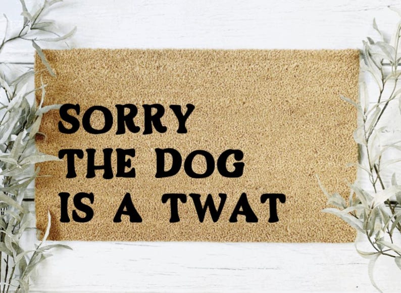 K&ouml;nnte beinhalten: Eine braune Fu&szlig;matte mit dem Text "SORRY THE DOG IS A TWAT" in schwarzen Buchstaben.