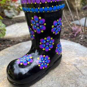 May include: Black painted ceramic rain boot planter with purple, blue and yellow polka dot flowers.