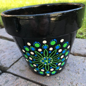 May include: Black terracotta flower pot with a white, green and blue dot mandala design.