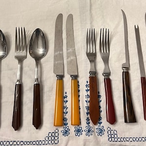 May include: A set of vintage cutlery with brown, red, and yellow plastic handles. The set includes forks, spoons, and knives.