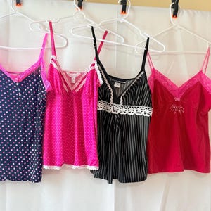 May include: Four different styles of pink and black lingerie tops with lace trim. The tops are hanging on hangers.