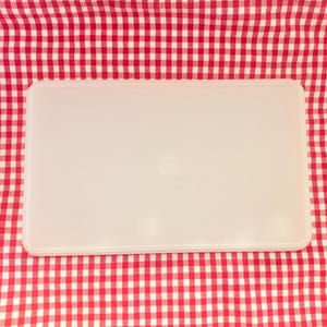 May include: A rectangular, off-white plastic container with rounded corners sits on a red and white checkered tablecloth. The container has a smooth, matte finish and a subtle logo in the center.