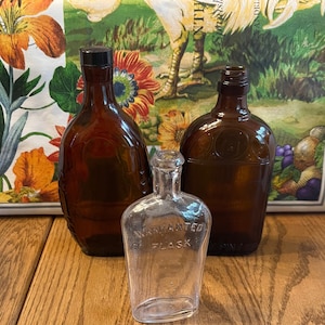 May include: Three glass bottles, two brown and one clear. The clear bottle is labeled "Warranted Flask".