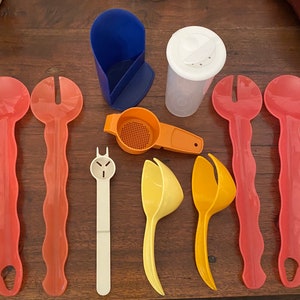 May include: A set of kitchen utensils including a blue plastic container, a white plastic shaker, a yellow plastic strainer, a white plastic tool with a face, two orange plastic strainers, and five pink plastic serving spoons.