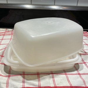 May include: A white plastic cake or bread storage container with a lid. The container is rectangular and has a smooth surface. The lid is slightly domed.