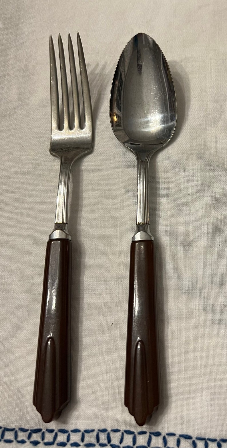 May include: A set of brown-handled silverware, including a fork and a spoon. The silverware is made of stainless steel and has a polished finish.