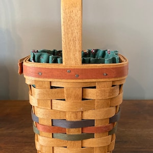 Pode incluir: Cesto tecido retangular com al&ccedil;a de madeira e faixas decorativas em tons de castanho, laranja e verde. O interior &eacute; forrado com tecido floral verde. Um item de armazenamento decorativo.
