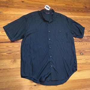 May include: A dark navy blue short-sleeve button-down shirt with a single chest pocket. The shirt has a classic collar and a relaxed fit. A small tag is attached to the collar.
