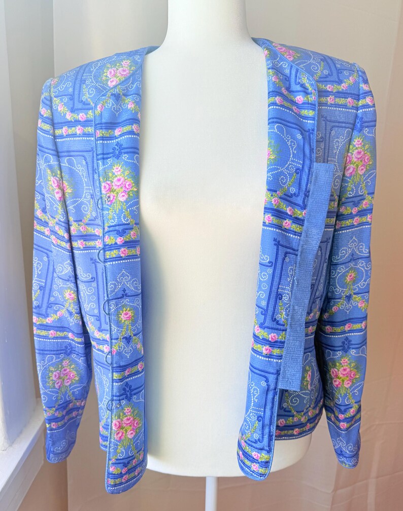 Puede incluir: Una chaqueta azul claro con un estampado floral con rosas rosas y un dise&ntilde;o paisley. La chaqueta tiene mangas largas y un cierre de un solo bot&oacute;n.