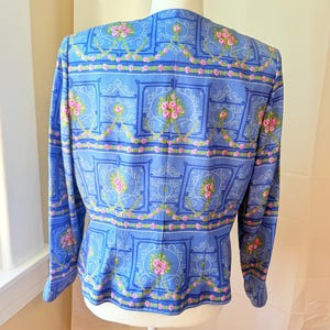 Puede incluir: Una chaqueta azul con un estampado floral con rosas rosas y dise&ntilde;os intrincados. La chaqueta tiene mangas largas y una cintura ajustada.