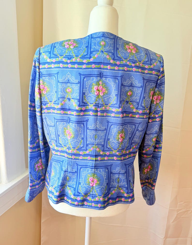 Puede incluir: Una chaqueta azul con un estampado floral con rosas rosas y dise&ntilde;os intrincados. La chaqueta tiene mangas largas y una cintura ajustada.