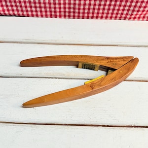 May include: A wooden nutcracker with a brass mechanism. The nutcracker is made of light brown wood and has a curved shape.