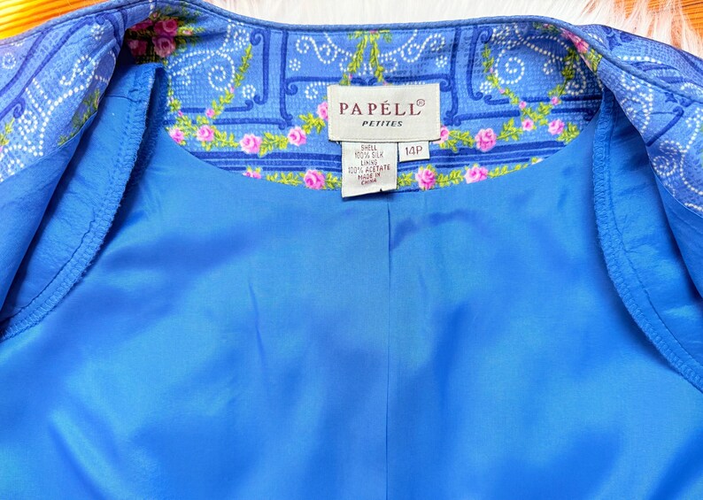 Puede incluir: Una chaqueta de seda azul con un forro de estampado floral. La etiqueta dice "Papell Petite" y "14P".