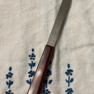 May include: A brown handled metal cheese knife with a forked tip.