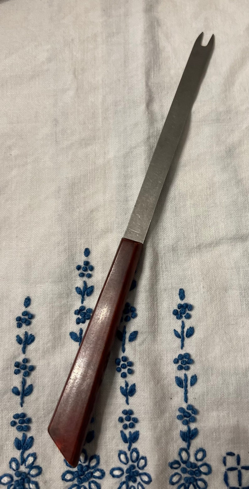 May include: A brown handled metal cheese knife with a forked tip.