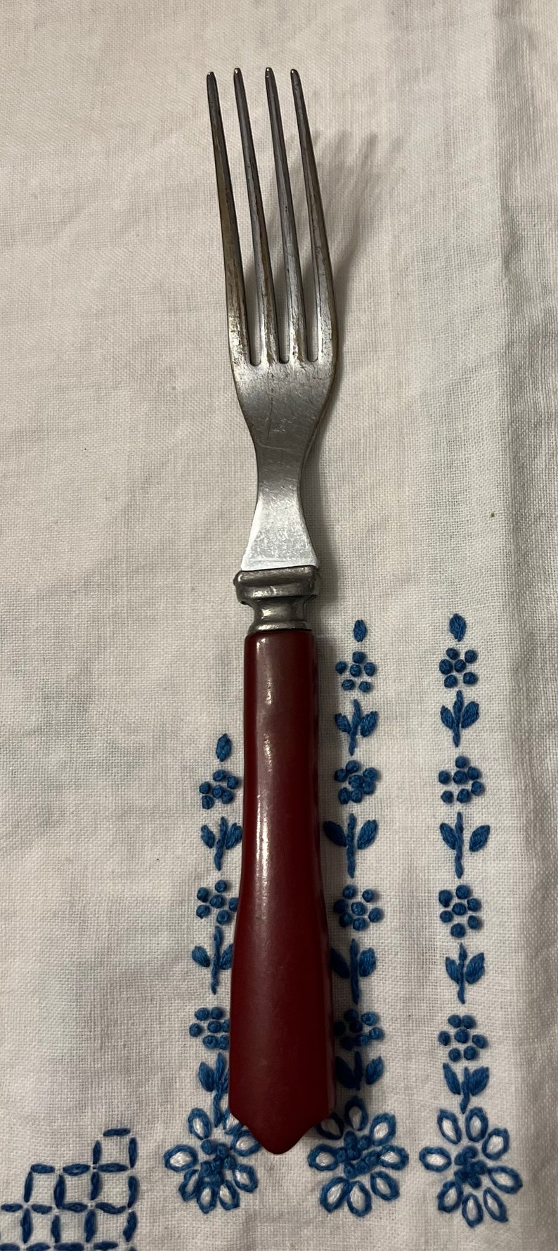 May include: A silver fork with a red plastic handle. The fork has four tines and a simple design.