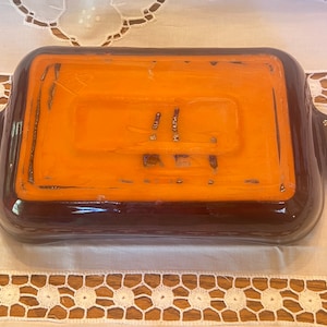 May include: A brown ceramic baking dish with a glazed orange interior. The dish has two handles on the sides.