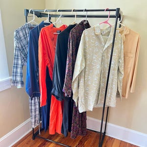 May include: A rack of clothing with a variety of patterns and colors, including a plaid shirt, a blue shirt, a red dress, a black dress, a floral dress, and a beige shirt.