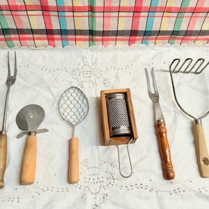 May include: A set of six kitchen utensils with wooden handles. The utensils include a fork, a potato masher, a pizza cutter, a wire whisk, a grater, and a fork with a long handle.