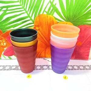 May include: A stack of colorful plastic cups in shades of red, yellow, and green on the left, and purple, pink, white, and orange on the right. The cups are set against a backdrop of a floral patterned fabric with large orange flowers and green leaves.