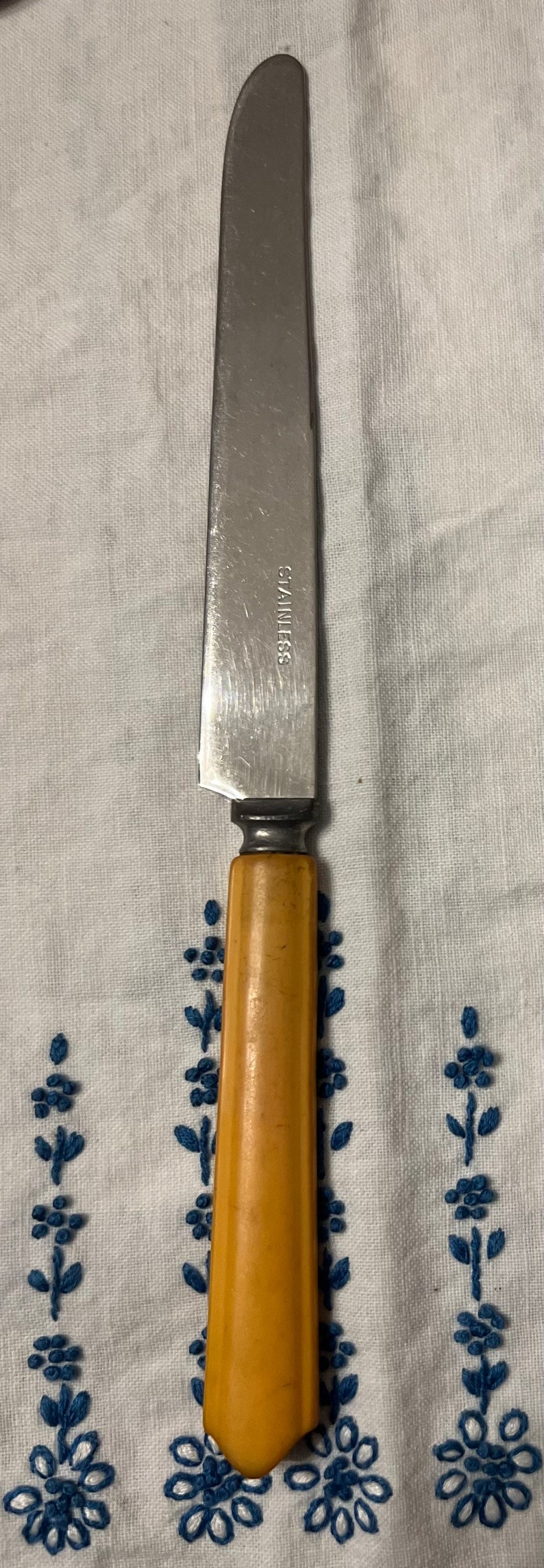 May include: A stainless steel butter knife with a yellow plastic handle. The knife has the word "STAINLESS" etched on the side.