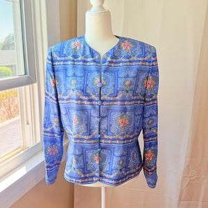 Puede incluir: Una chaqueta azul con un estampado floral con rosas rosas y fondo blanco. La chaqueta tiene cierre de botones y mangas largas.