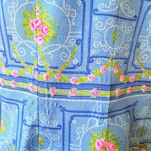 Puede incluir: Tela azul con un dise&ntilde;o estampado blanco y azul con rosas rosas. La tela tiene una textura acolchada.