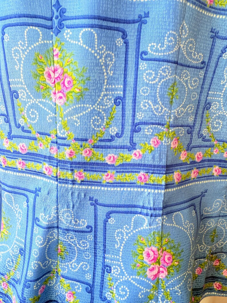 Puede incluir: Tela azul con un dise&ntilde;o estampado blanco y azul con rosas rosas. La tela tiene una textura acolchada.