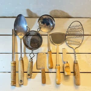 May include: A collection of eight kitchen utensils, including a slotted spoon, a ladle, a whisk, a strainer, a spatula, a spoon, a slotted spoon, and a wire whisk. The utensils are all made of metal and have wooden handles.