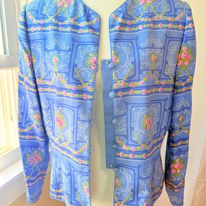 Puede incluir: Una chaqueta azul claro con un estampado floral con rosas rosas y fondo blanco. La chaqueta tiene cierre de botones y mangas largas.