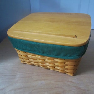 May include: A woven basket with a wooden lid and a green fabric liner. The lid has a small wooden handle.